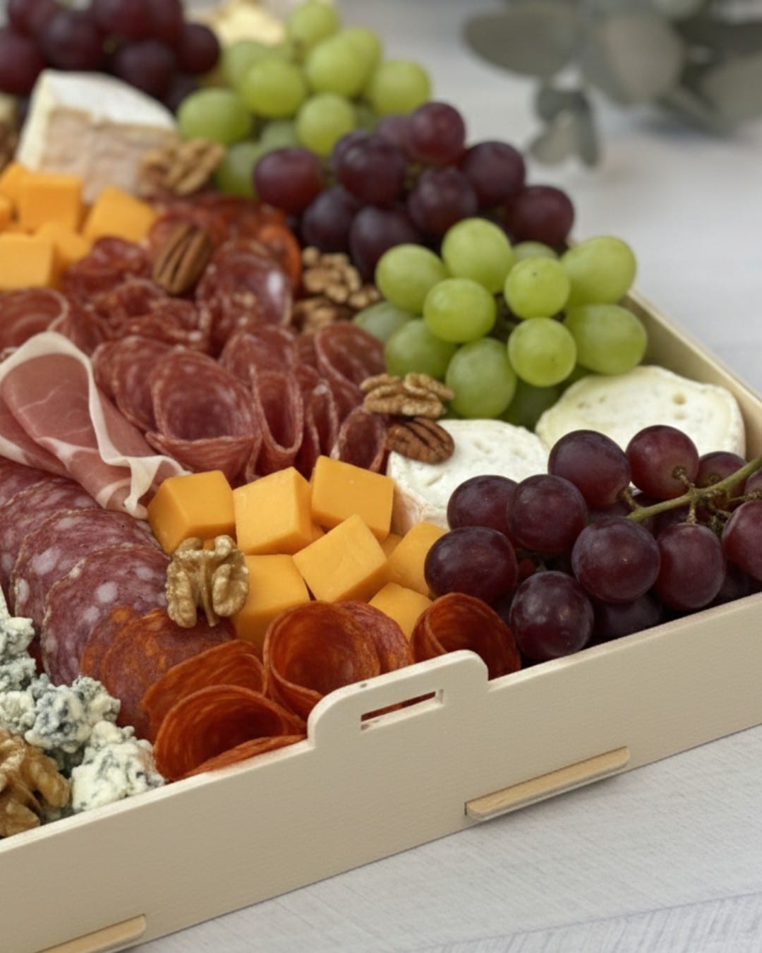 Bandeja de madera Sincla con asas llena de embutidos, quesos, uvas y nueces