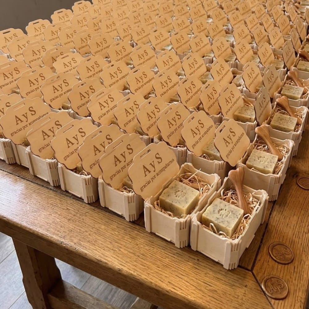 Decenas de cajitas de madera Sincla con «AyS» y «gracias por acompañarnos» grabados en la tapa, sobre una mesa