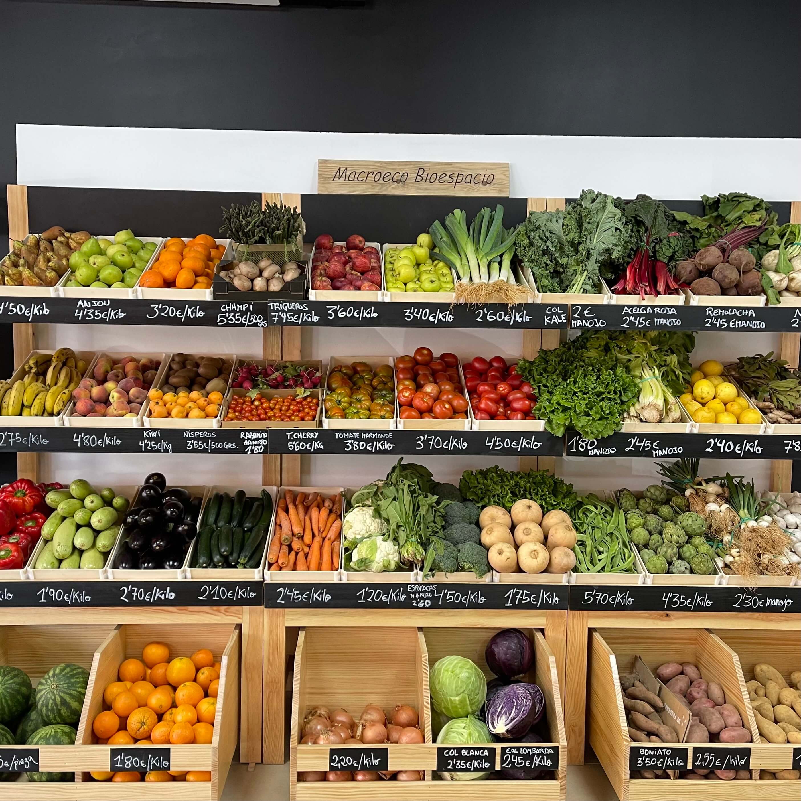 Estanterías de una frutería con cajas de madera Sincla llenas de fruta y verdura, con los precios en pizarras