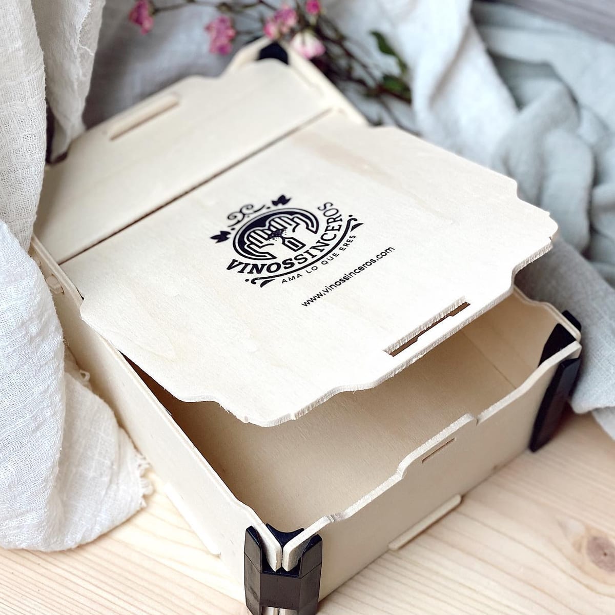 Caja con bisagra entreabierta con el logo de una vinoteca impreso en negro en la tapa