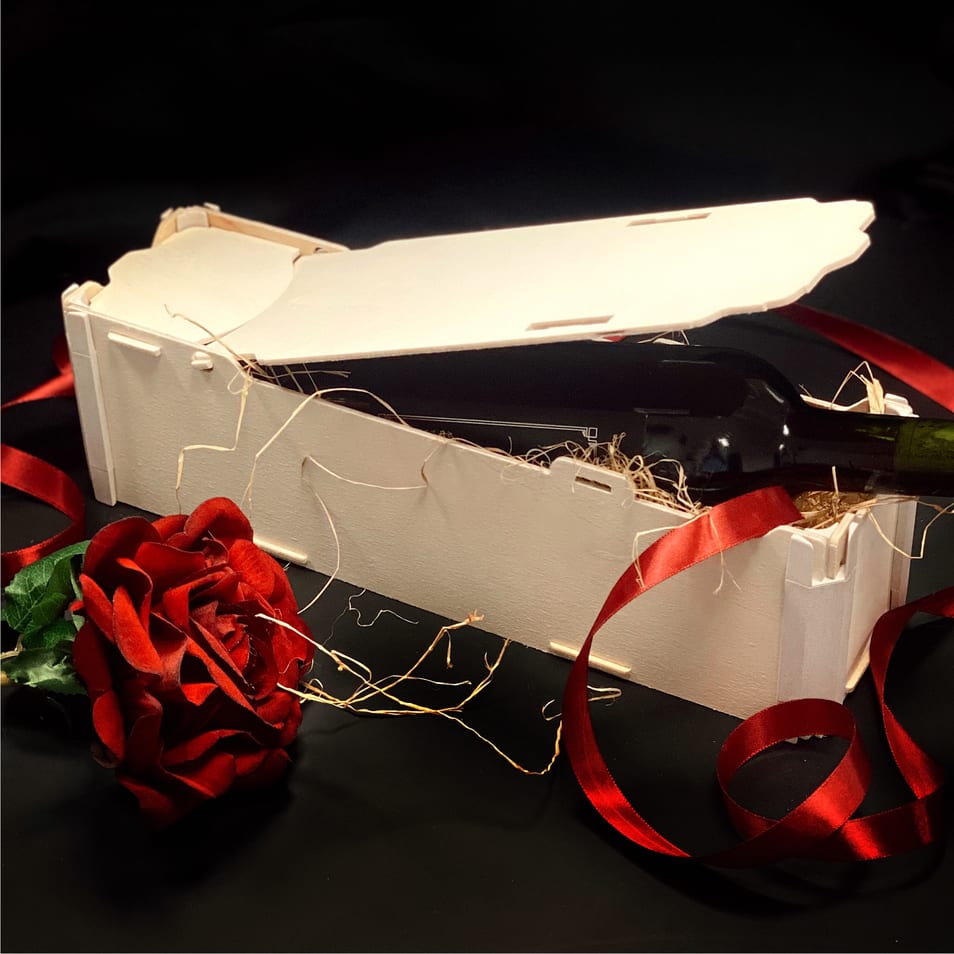Caja de madera para una botella tumbada con la tapa entreabierta, una rosa roja y cinta roja sobre fondo negro