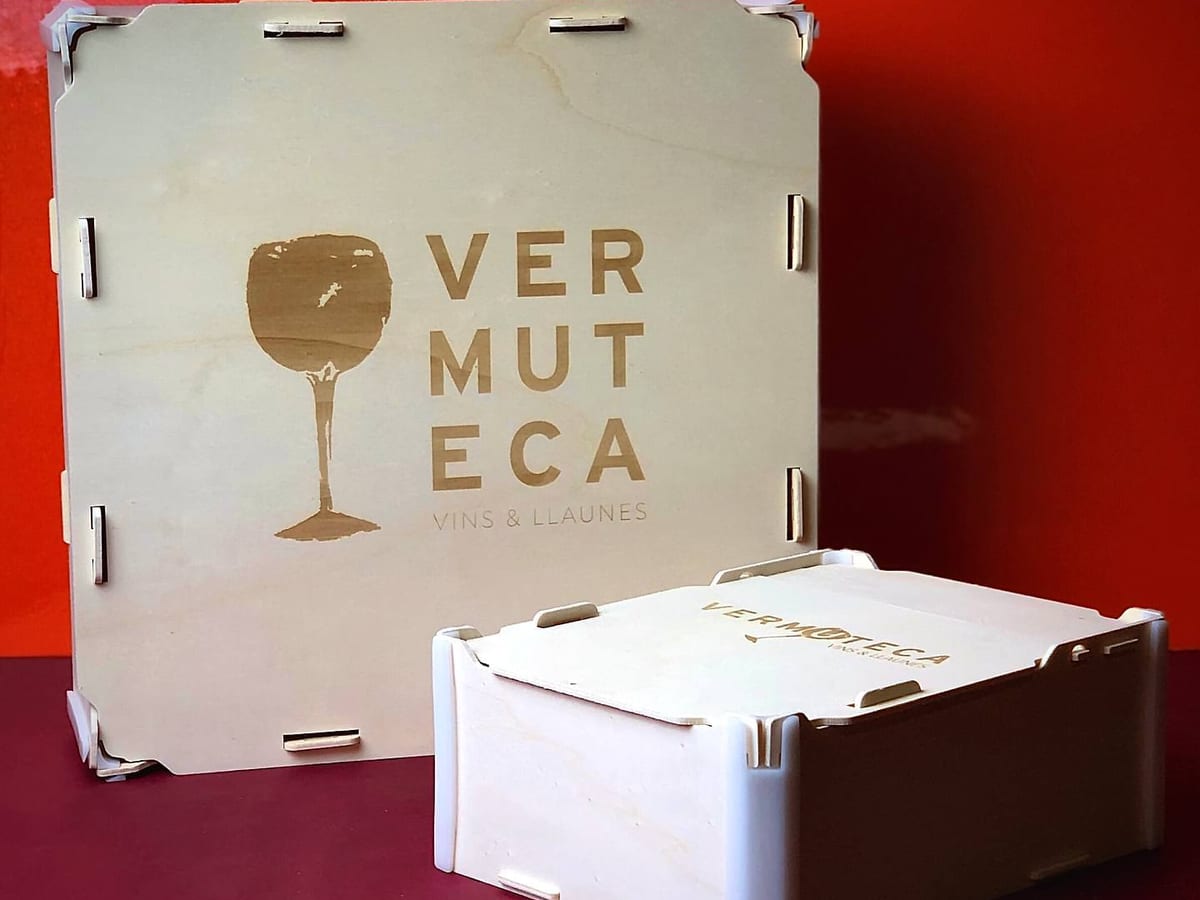 Caja con tapa de madera con el logo de una vermutería grabado (una copa y su nombre), junto a una caja más pequeña con el mismo logo